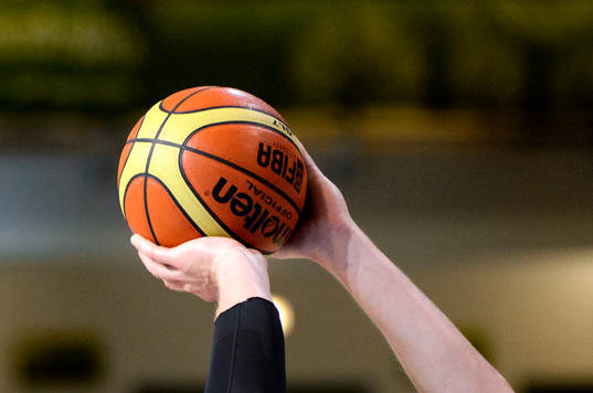En basketboll i händerna på en spelare i matchen mellan