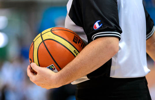 En basketboll i handen på en domare i matchen mellan
