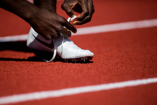An athlete ties his shoelaces in the men's 100m heats