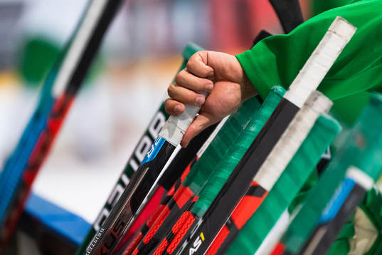 En hand tar en ishckeyklubba som står lutad mot sargen på