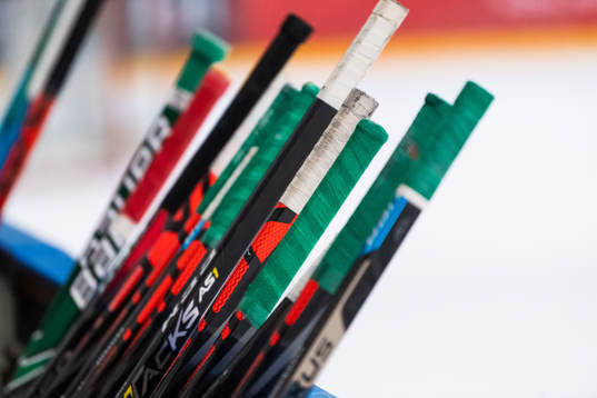 Ishockeyklubbor står lutade mot sargen på en träning med