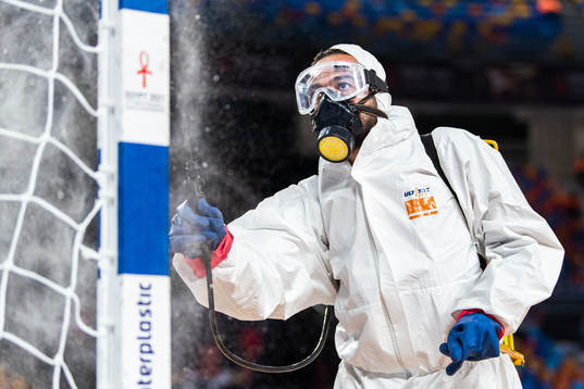A person in protective gear disinfects a goalpost, due to