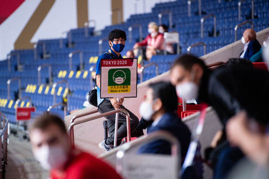 An official with a sign telling people to wear a facemask