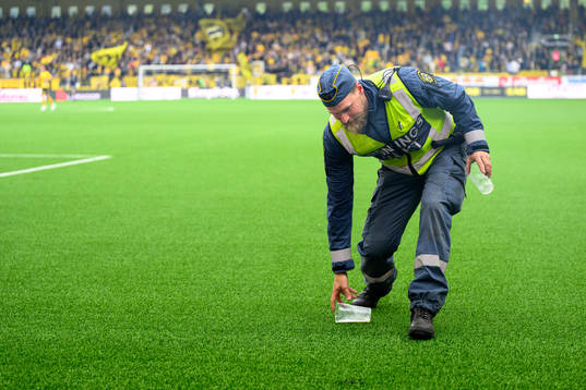 En ordningsvakt plockar upp inkastade föremål från planen