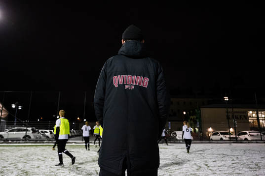 En ledare med klubbnamnet på jackan tittar på spelare