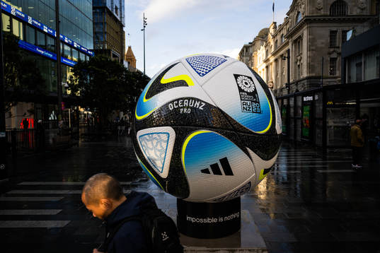 People walk past a replica of the official match ball
