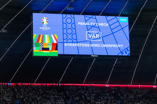 A big screen displays a VAR review message